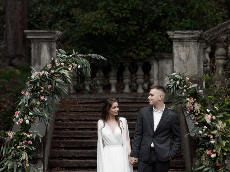 Round wedding arch, decorated with white flowers and greenery, in front of the old Italian architecture. A wedding in an old villa, a happy couple of newlyweds