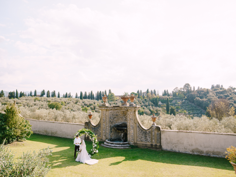 Wedding at an old winery villa in Tuscany, Italy. Wedding couple under a round arch of flowers. The groom reads wedding vows