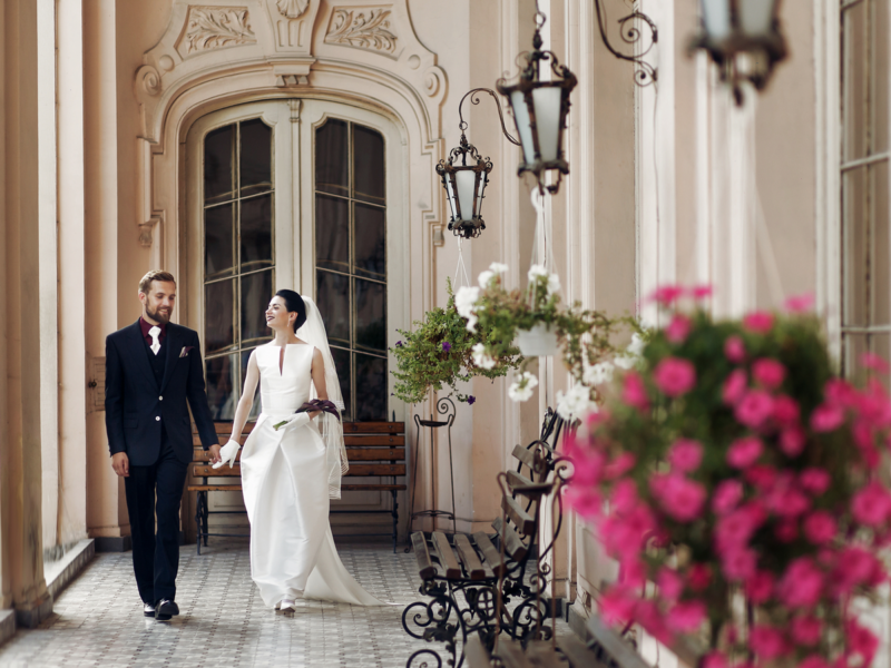 elegant gorgeous bride and stylish groom walking holding hands, sensual touch on background of old building. unusual luxury wedding couple in retro style