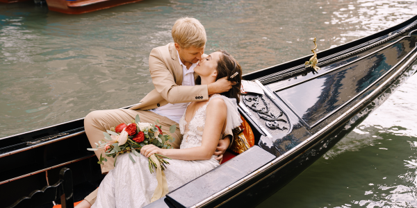Italy wedding in Venice. The bride and groom ride in a classic wooden gondola along a narrow Venetian canal. Close-up of cuddles newlyweds