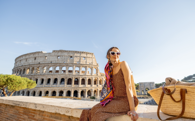 Portrait of a cheerful woman on background of Coliseum in Rome on a summer time. Concept of visiting famous landmarks and travel Italy. Girl wearing dress and colorful shawl Imagine-se vivendo a Itália com suporte total, aproveitando despreocupada cada instante.
