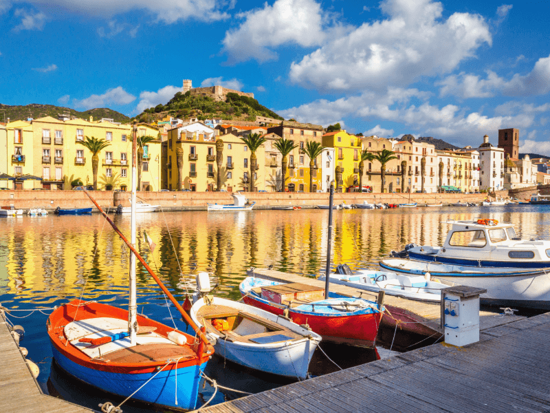 Descubra a magia colorida de Bosa, onde barcos tradicionais dançam nas águas douradas.